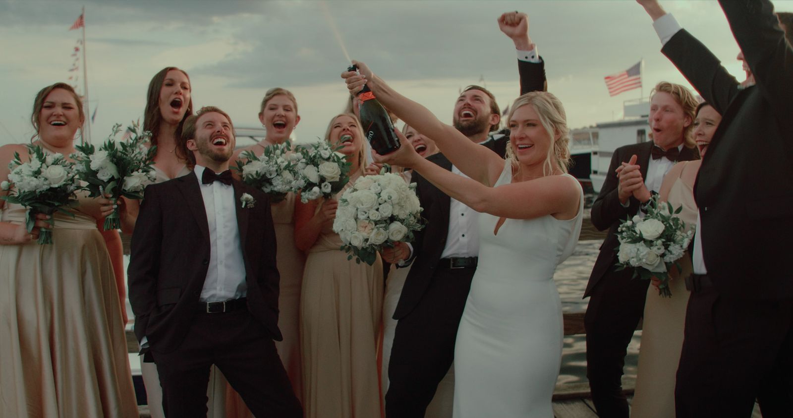 Bride spraying champagne with her wedding party on a dock